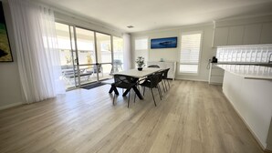 Et moderne køkken med hvide skabe, et spiseområde med bord og stole, og udsigt gennem store glasdøre til en udendørs terrasse.