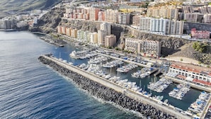 A coastal cityscape with a marina filled with boats, surrounded by residential buildings and hills in the background.