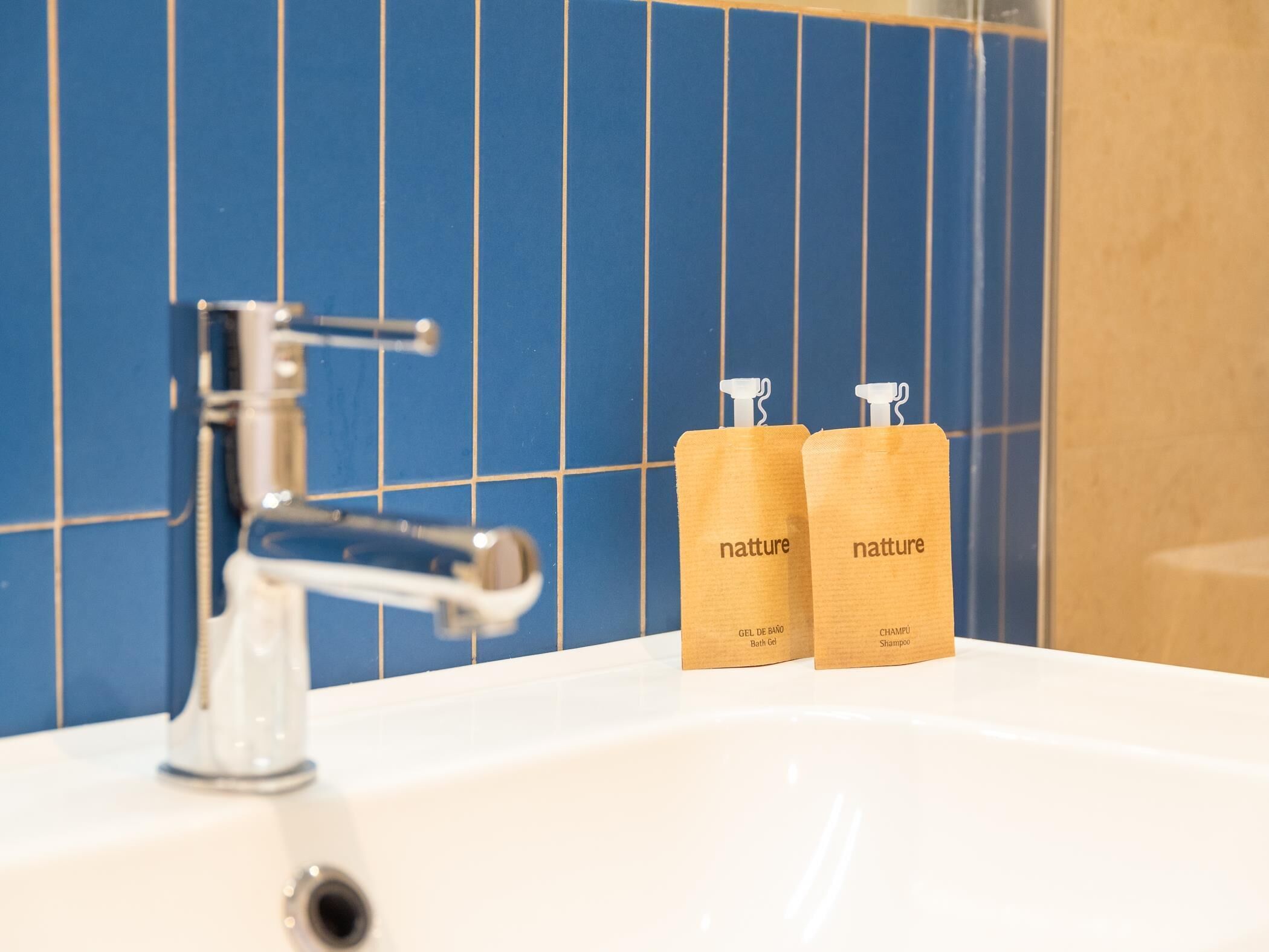 Ein Badezimmer mit einem weißen Waschbecken, einem chromfarbenen Wasserhahn und zwei Holzflaschen mit dem Aufdruck 'natture', gefüllt mit Badesalz und Shampoo.