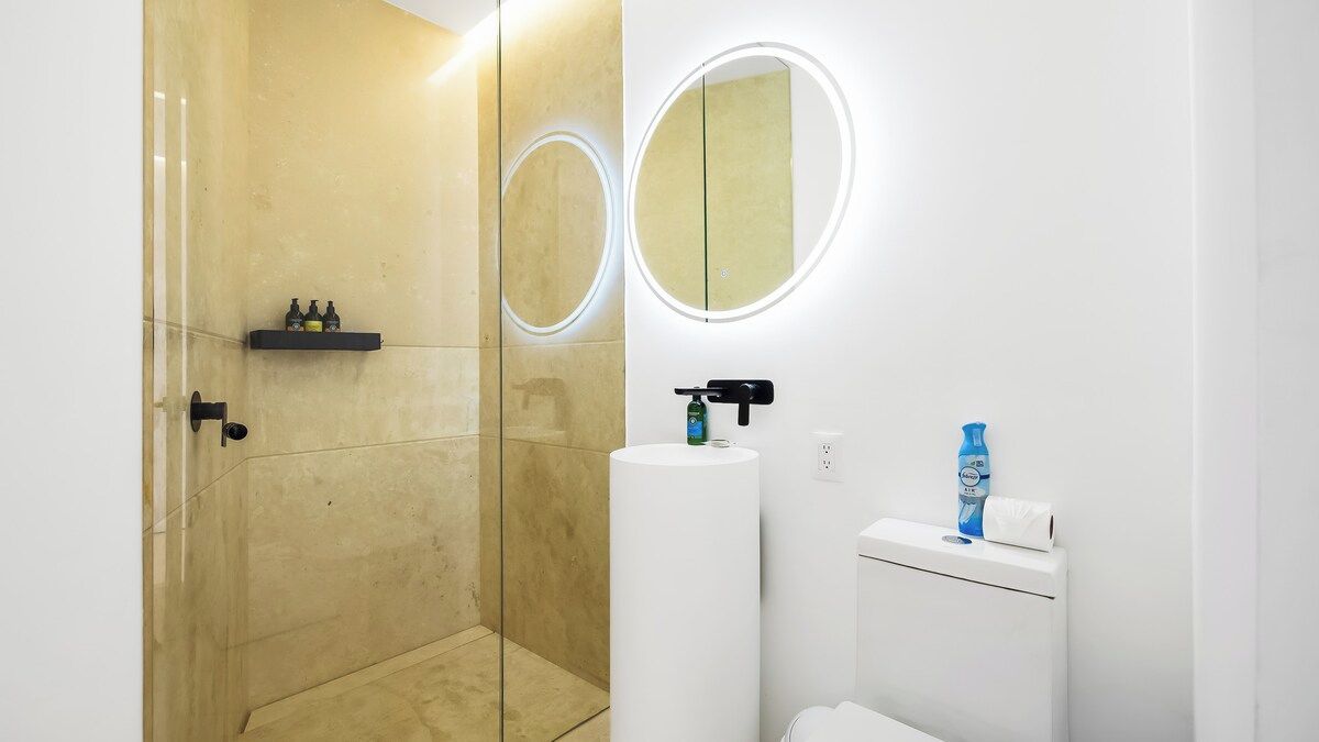 A modern bathroom with a glass shower enclosure, a white sink with a mirror, and a toilet.