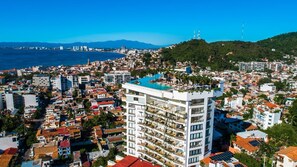 A high-rise hotel with multiple balconies, a rooftop pool, and a view of the city and sea.