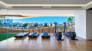 A modern gym with treadmills and an elliptical machine, large windows with a city view.