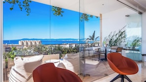 A balcony with a clear view of the sea and buildings, furnished with a sofa and chairs.