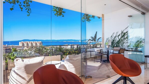 A balcony with a clear view of the sea and buildings, furnished with chairs and a table.