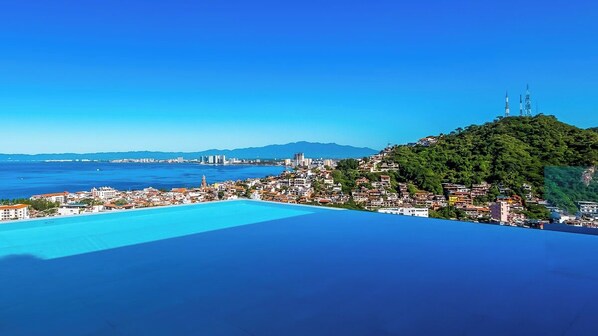 Un paisaje urbano costero con vista despejada al mar, una colina con edificios y una torre destacada.