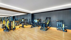 Un gimnasio moderno con diversas máquinas de ejercicio, suelo de madera y pared oscura.