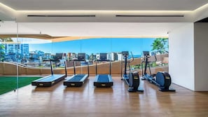 Une salle de sport moderne équipée de tapis de course, de vélos elliptiques et d’un rameur, et dotée de grandes fenêtres offrant une vue sur la ville.