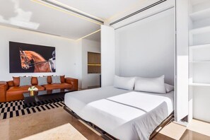 A modern bedroom with a large bed, a sofa, and a mounted painting.