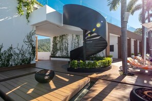Un espacio exterior moderno con una escalera espiral, terraza de madera y plantas en macetas.
