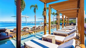 A poolside area with lounge chairs and umbrellas, overlooking a body of water with a clear sky.