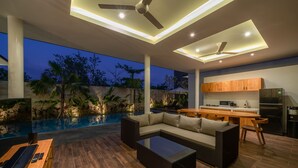 Et moderne udendørs opholdsområde med swimmingpool, sofa, spisebord og et køkken.