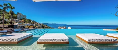 A poolside area with lounge chairs and a view of the ocean.