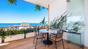 A balcony with a round table and chairs, overlooking a coastal cityscape.