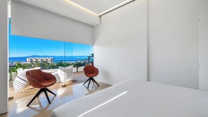 A modern bedroom with a large window, a bed, and two chairs.