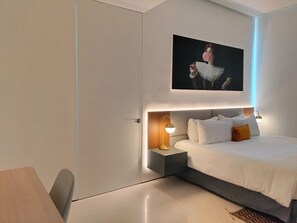 A modern hotel room with a bed, bedside tables, and a painting on the wall.