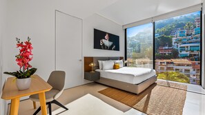 A modern bedroom with a large bed, a desk, and a potted orchid.