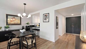 Una cocina moderna con armarios blancos, una mesa de comedor con sillas y una puerta negra al fondo.