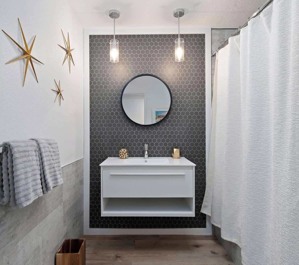 A bathroom with a white vanity, a round mirror, and a hexagonal patterned wall.