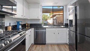 Una cocina moderna con armarios blancos, electrodomésticos de acero inoxidable y un amplio ventanal con vistas al exterior.