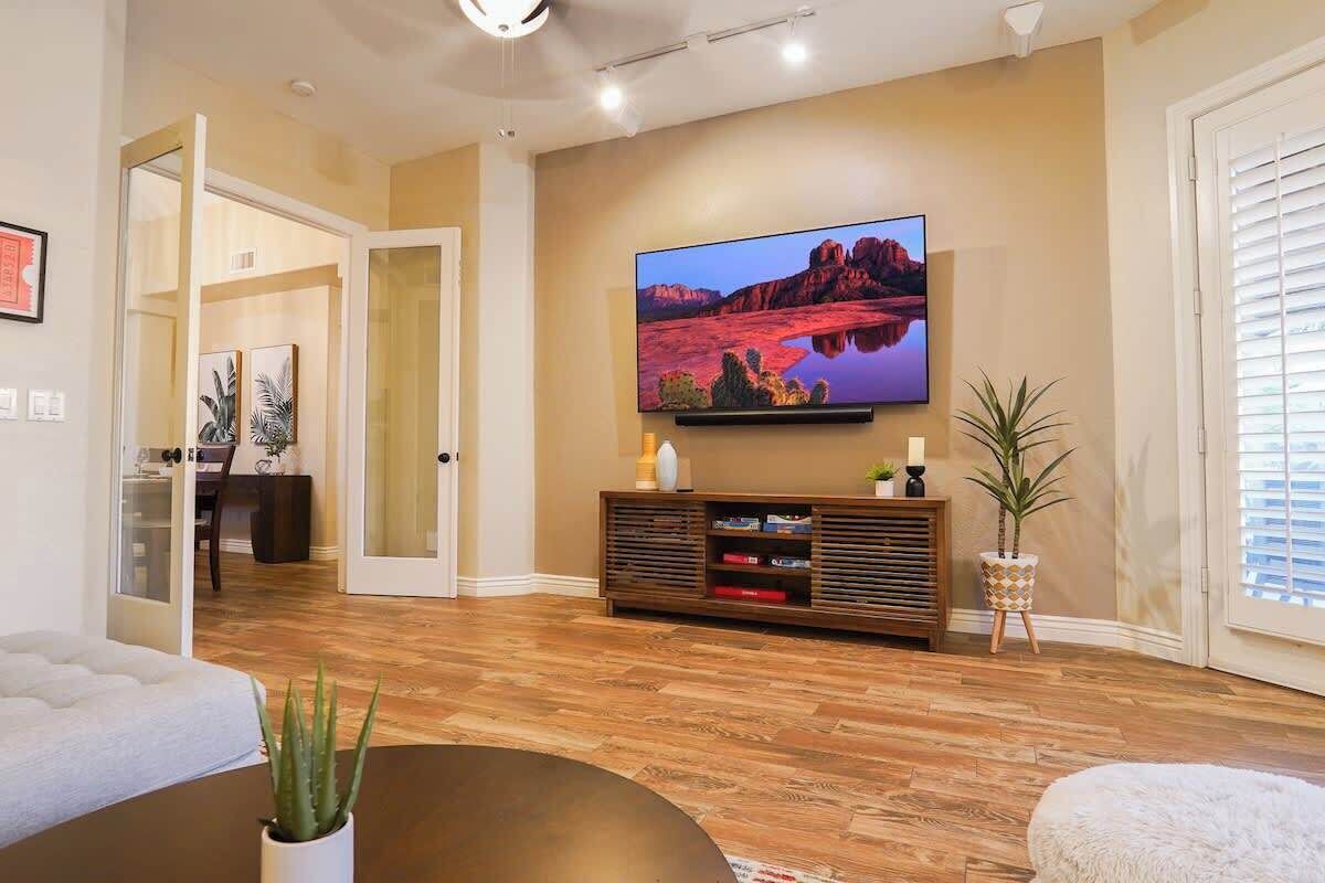 A living room with a flat-screen TV, wooden flooring, a sofa, a coffee table, and a potted plant.
