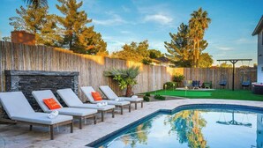 Un patio trasero con piscina, sillas de descanso y una valla de madera.