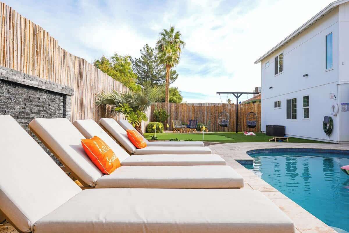 A poolside area with lounge chairs, a wooden fence, and a white building in the background.