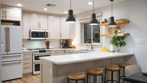 Cocina moderna con armarios blancos, una isla central con taburetes, iluminación colgante y una ventana sobre el fregadero.
