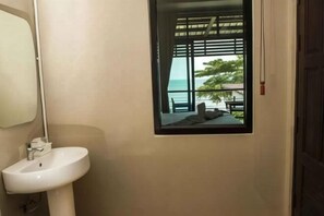 Un bagno con un lavandino bianco, uno specchio e una finestra vista mare e palme.