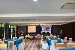 A banquet hall with tables set for a formal event, a stage with a banner, and a checkered floor. - Sea Stone Hotel Sichon (Sichon)