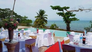 Ein Essbereich im Freien mit gedeckten Tischen für eine Hochzeit, mit Blick aufs Meer.