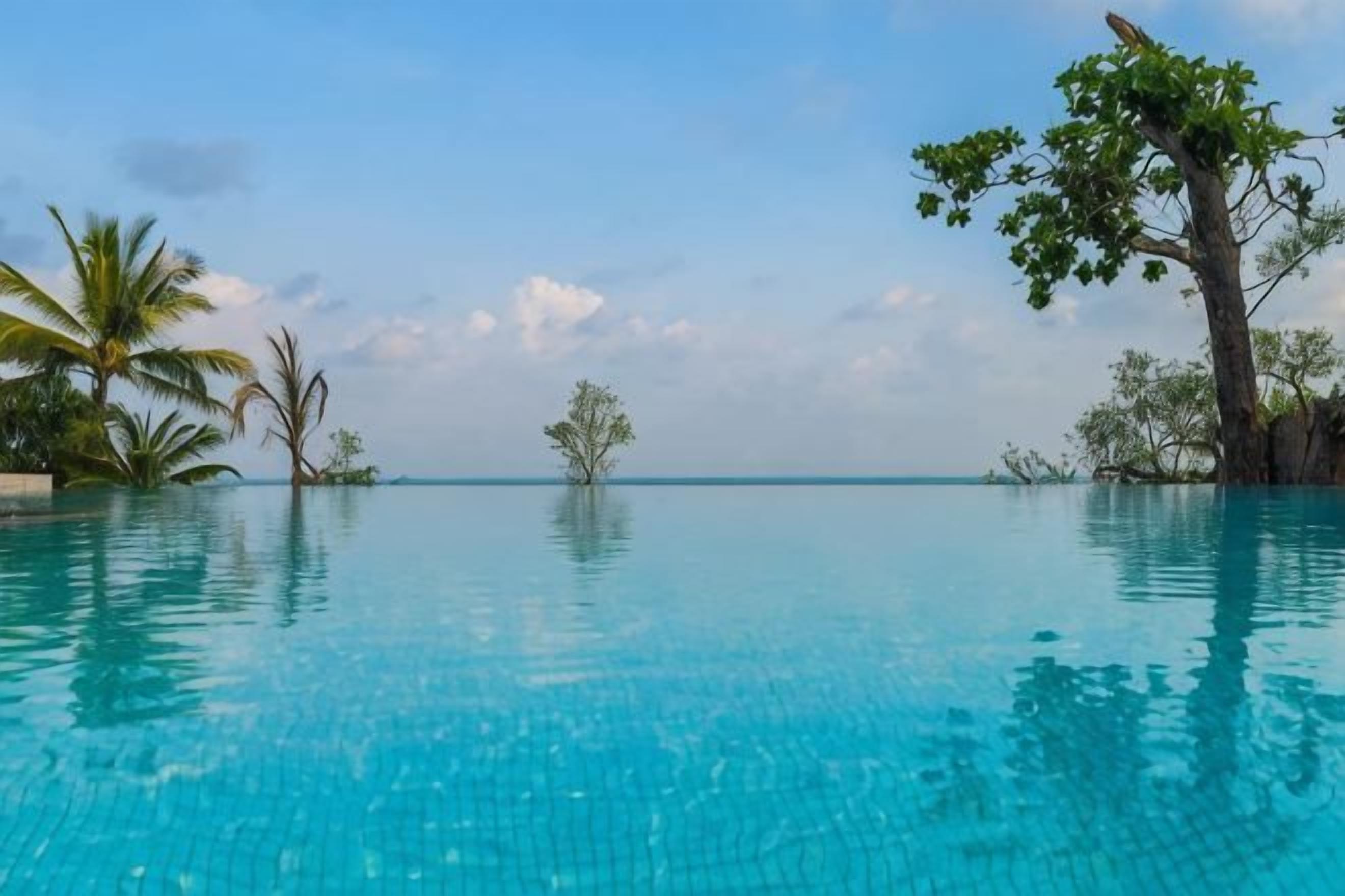 Una piscina azul y cristalina con agua tranquila, rodeada de vegetación tropical y un cielo despejado.