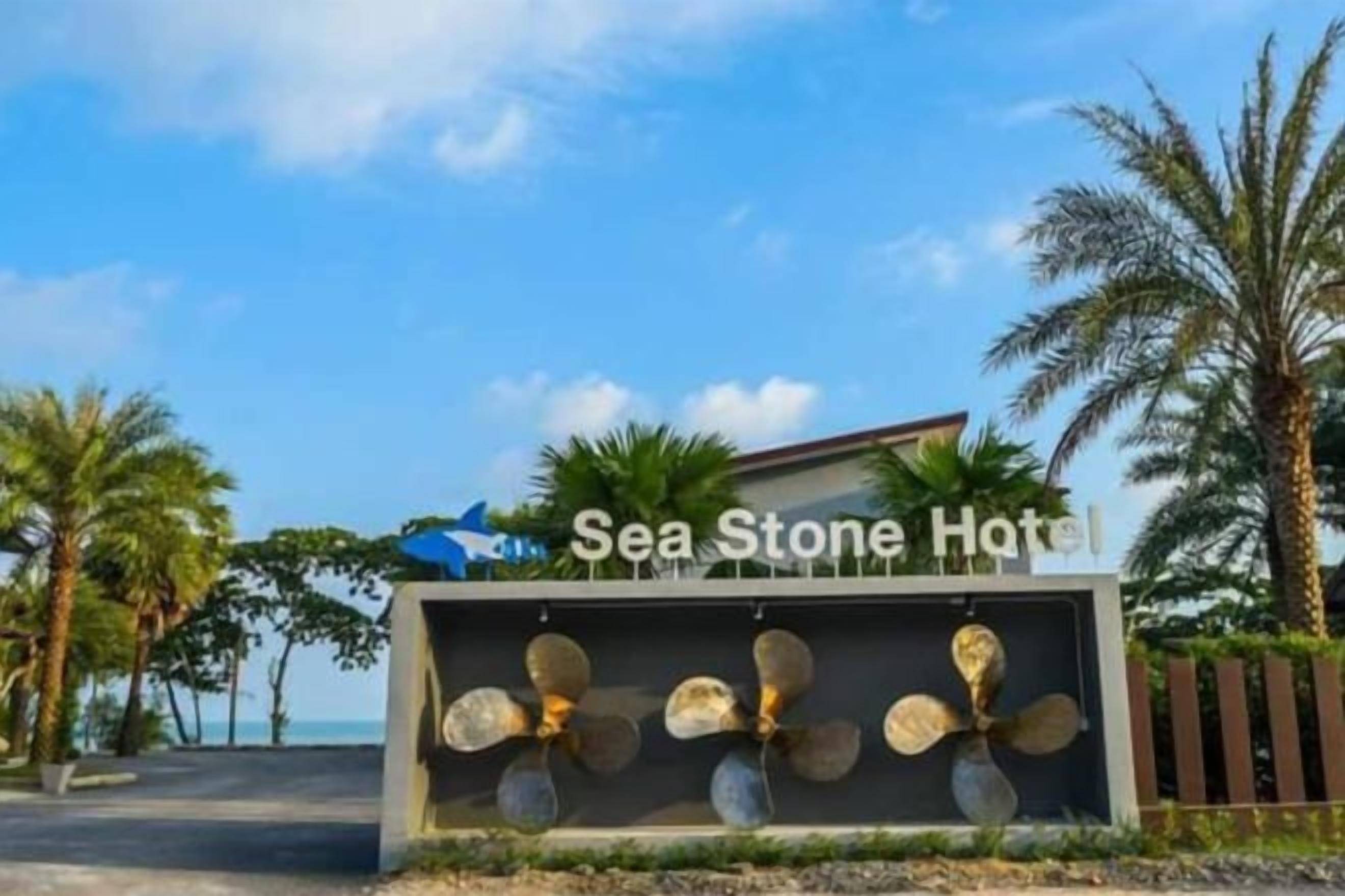 Señal para Sea Stone Hotel, con un abanico decorativo y palmeras al fondo.