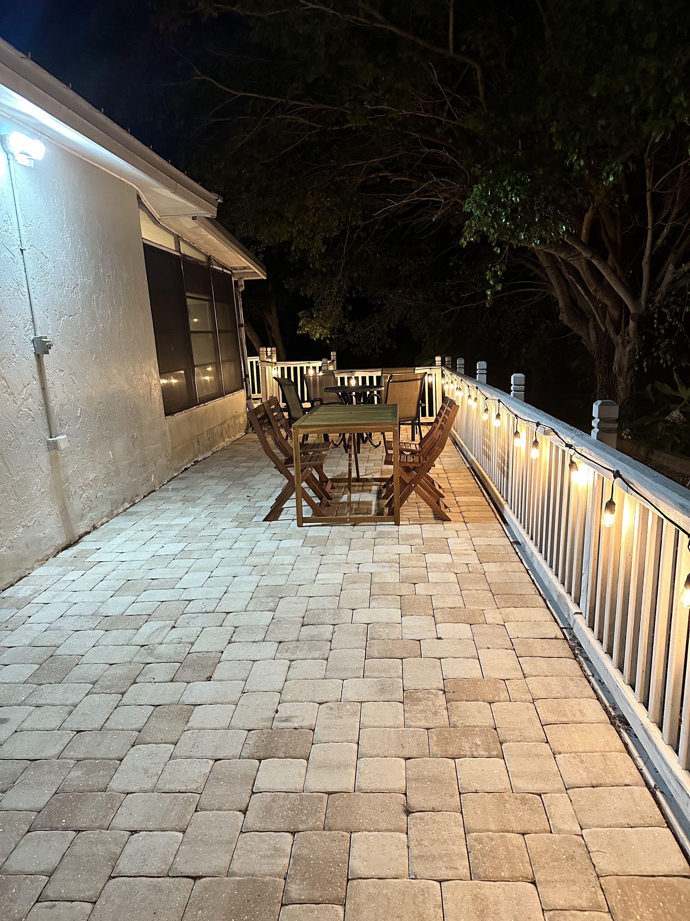 Un patio con una mesa y sillas, una barandilla y un edificio al fondo.
