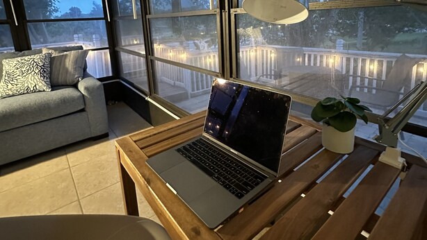 A modern room with a large window, a laptop on a wooden table, a sofa, and a floor lamp. - New Beach Cabana with Mini Golf (Venice)