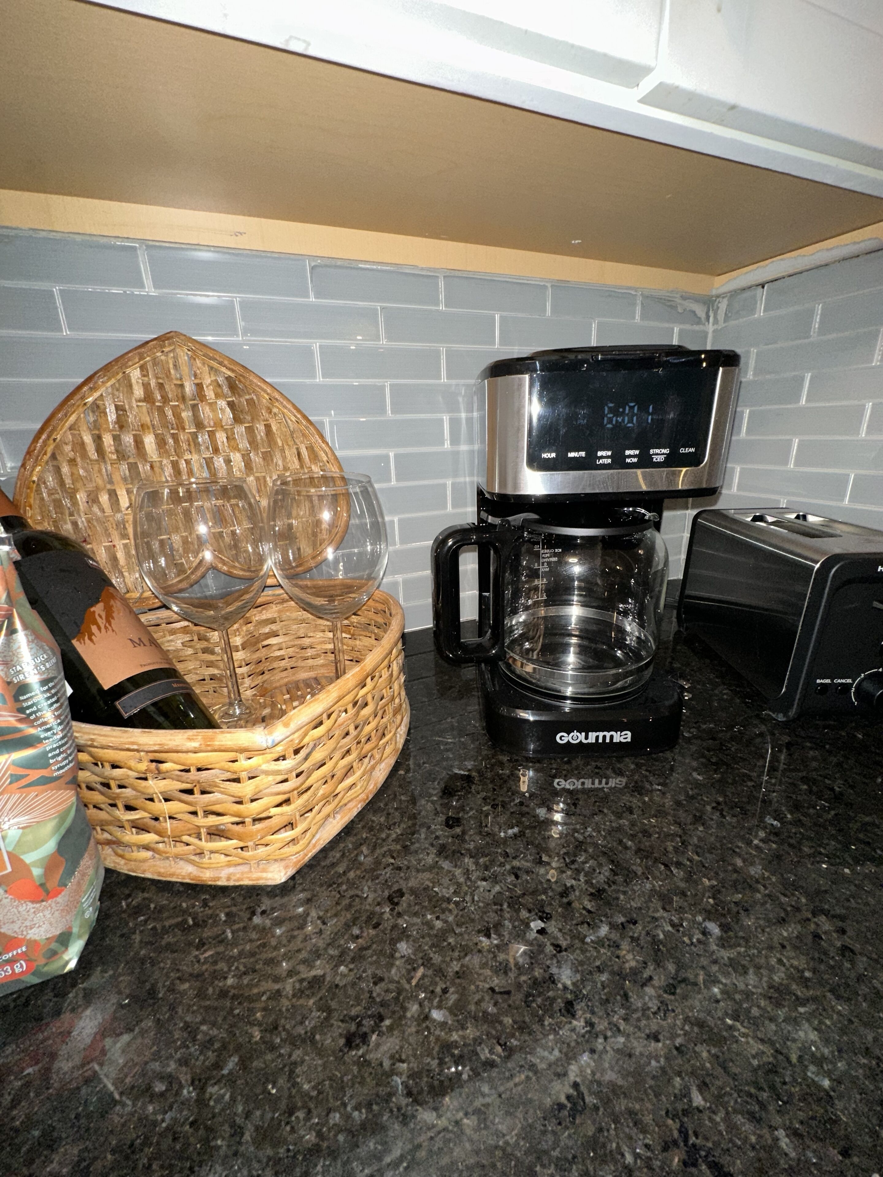 Una cocina con cafetera, una cesta con copas de vino y una botella de vino.