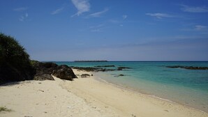 En strand med kristallklart turkost vatten, en sandstrand och klippiga utskjutande partier.