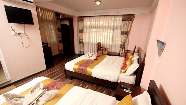 A hotel room with two beds, a TV, and a window with curtains. - De Hotel Veda (Kathmandu)