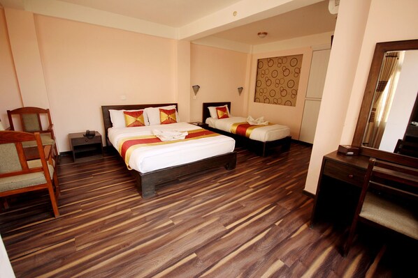 A hotel room with two beds, wooden flooring, a desk, a chair, and a mirror. - De Hotel Veda (Kathmandu)