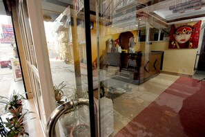 A hotel lobby with a reception desk, a staircase, and a view of the street outside. - De Hotel Veda (Kathmandu)