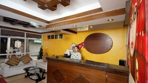A hotel reception area with a wooden reception desk, a Christmas tree, and a sign indicating check-out time. - De Hotel Veda (Kathmandu)