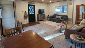 Una sala de estar acogedora con techo de madera, televisor, sofá y mesa de comedor con sillas.