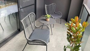 A balcony with two wicker chairs and a small table, a potted plant, and a glass door leading to an interior space. - CBD Elizabeth St Modern Townhouse - Secure Parking (Launceston)