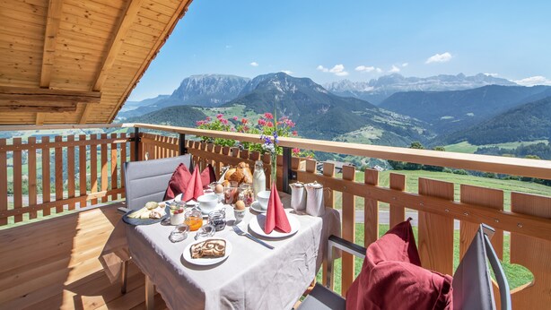 A wooden deck with a table set for breakfast, overlooking a mountainous landscape.