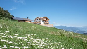 A two-story house with a balcony, situated on a grassy hill with a clear view of the surrounding landscape.