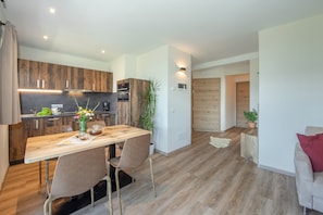 A modern kitchen with wooden cabinets, a dining table with chairs, and a living area with a sofa.