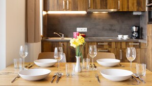 A dining table set with white plates, bowls, and cutlery, a vase with yellow flowers, and a wooden kitchen in the background.