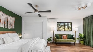 A bedroom with a bed, a green sofa, a ceiling fan, a window with curtains, and a wall-mounted air conditioner. - Manzanita Rest (Mariposa County)