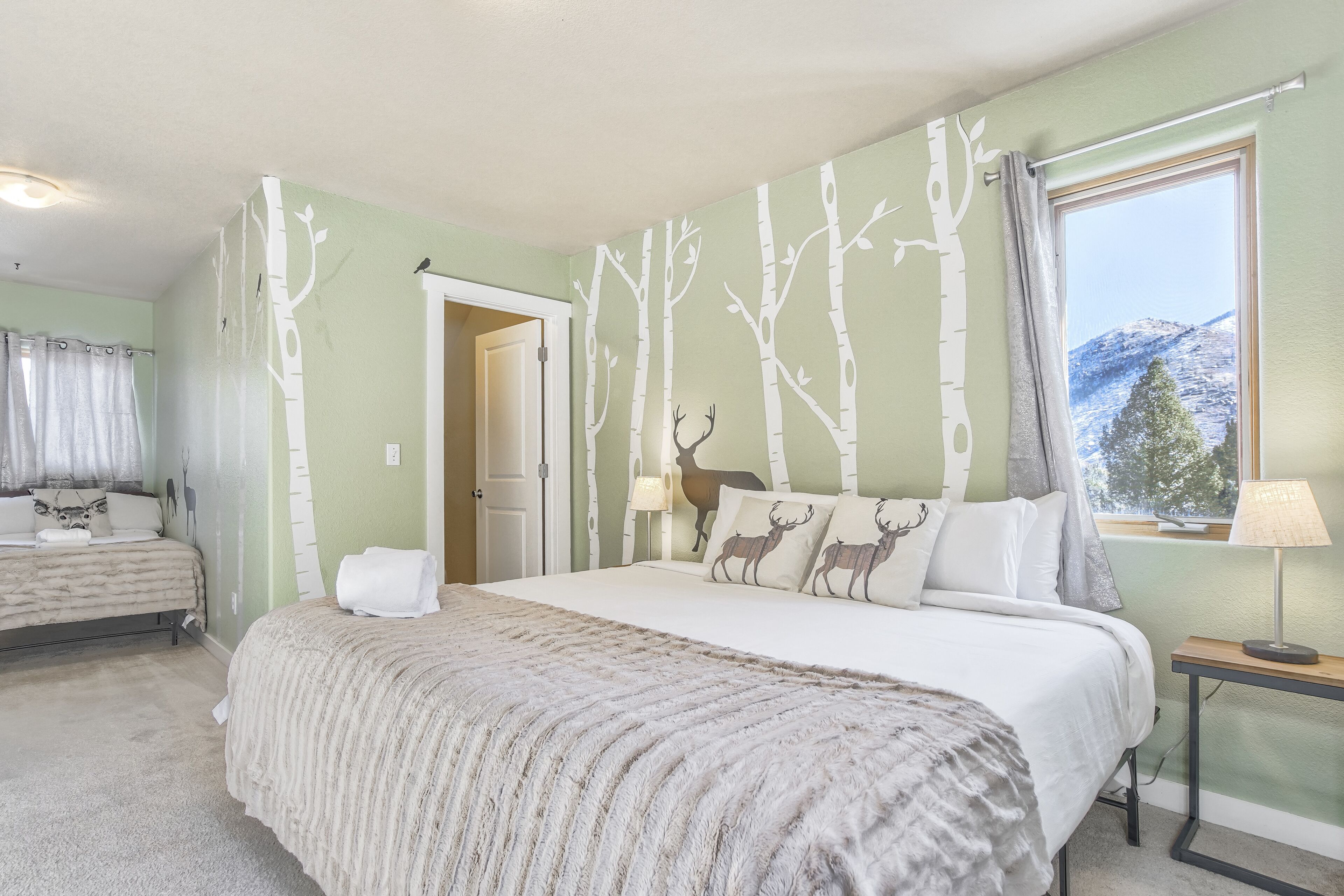 Une chambre avec un grand lit, une table de chevet, une fenêtre donnant sur la montagne et une porte menant à une autre pièce.