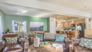 A spacious living room with leather sofas, a coffee table with board games, and a view of the kitchen in the background. - Peekaboo Mountain (Cascade)