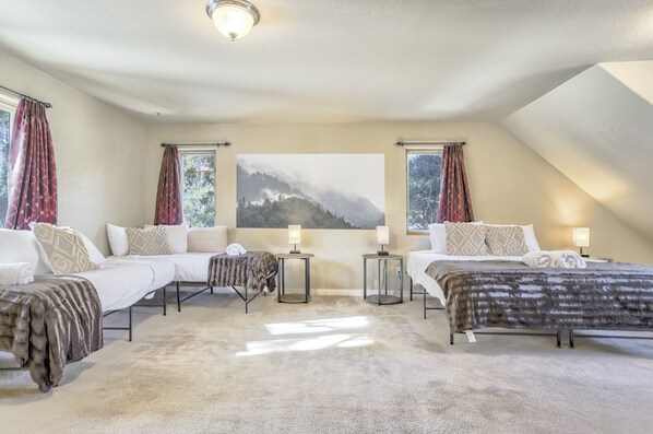 A bedroom with two beds, a large window with curtains, a painting of a mountain, and a ceiling light. - Peekaboo Mountain (Cascade)